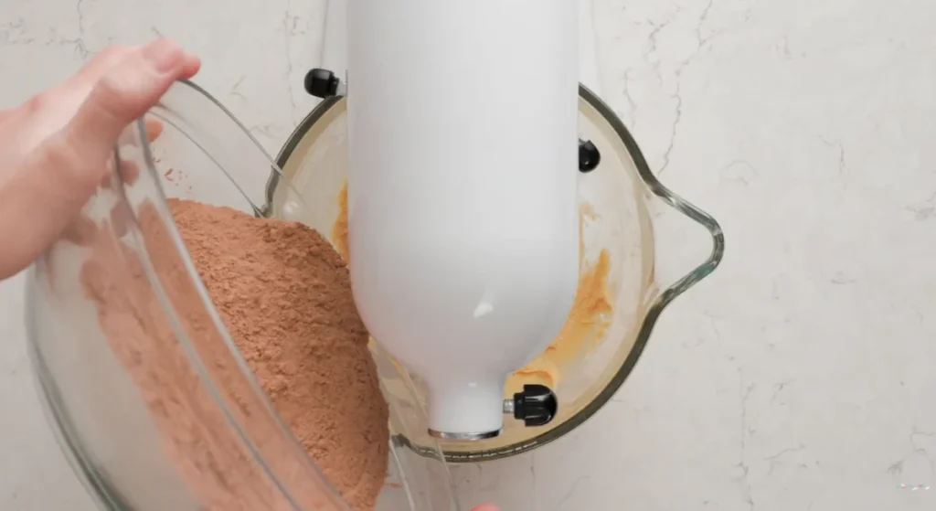 Dry chocolate cookie ingredients being added to the wet mixture