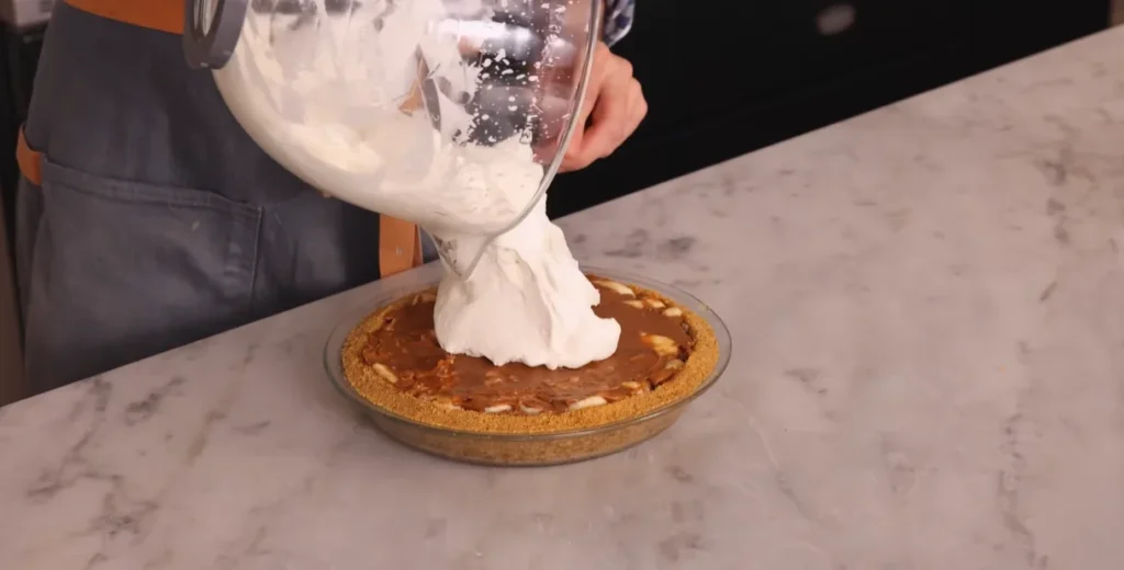 Whipped cream being added over the banana layer of Banoffee Pie