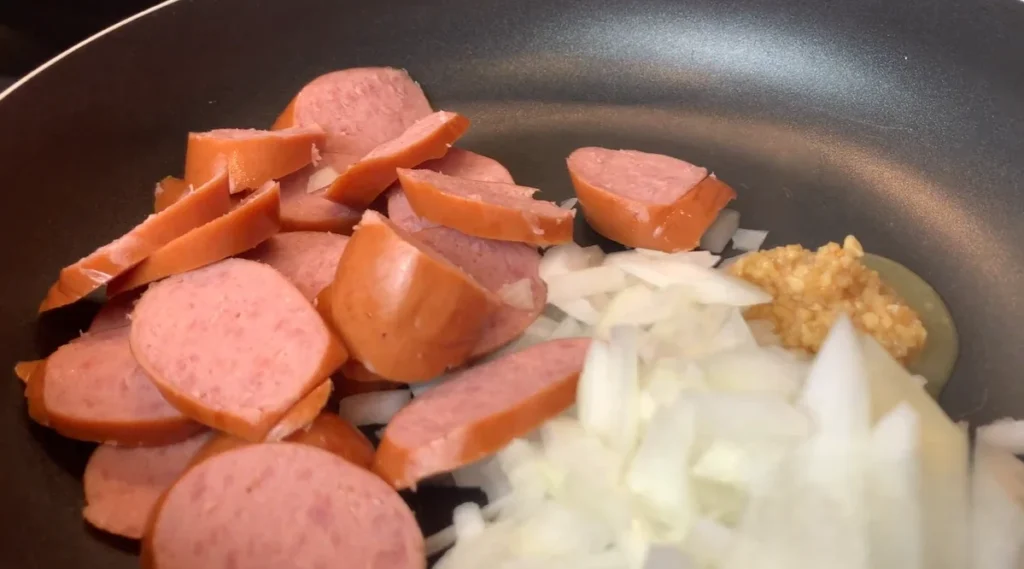 Sliced smoked sausage cooking with diced onion and garlic in a skillet