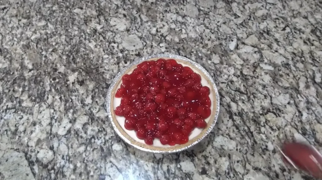 Cherry pie filling spread over chilled cream cheese layer in graham cracker crust