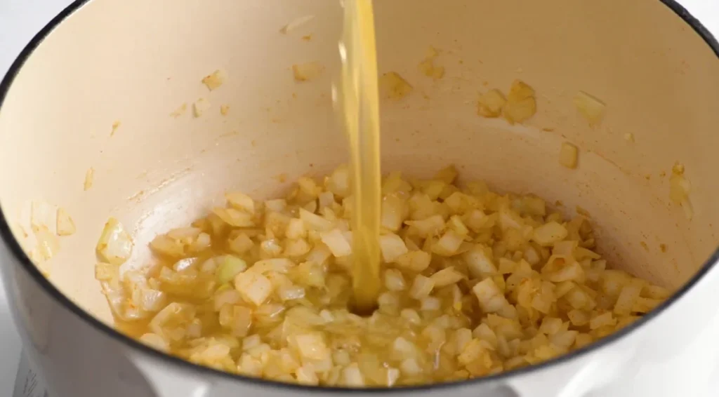 Chicken broth poured into the sautéed onion and seasoning mixture