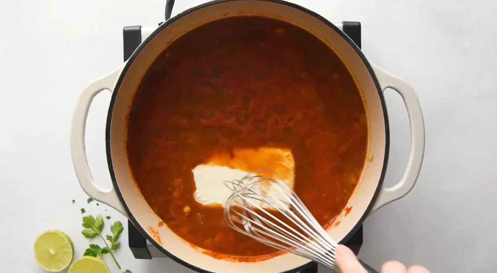 Cream cheese being whisked into the chicken enchilada soup for a creamy finish
