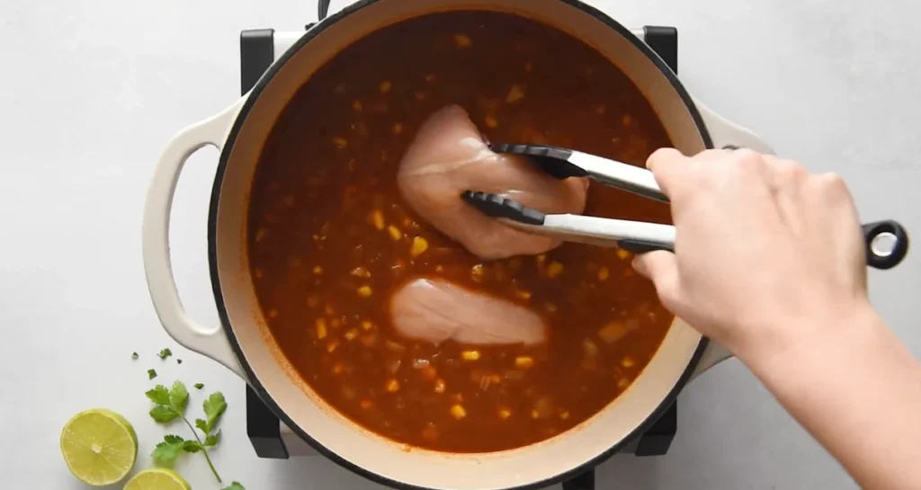 Raw chicken breasts added to the simmering chicken enchilada soup