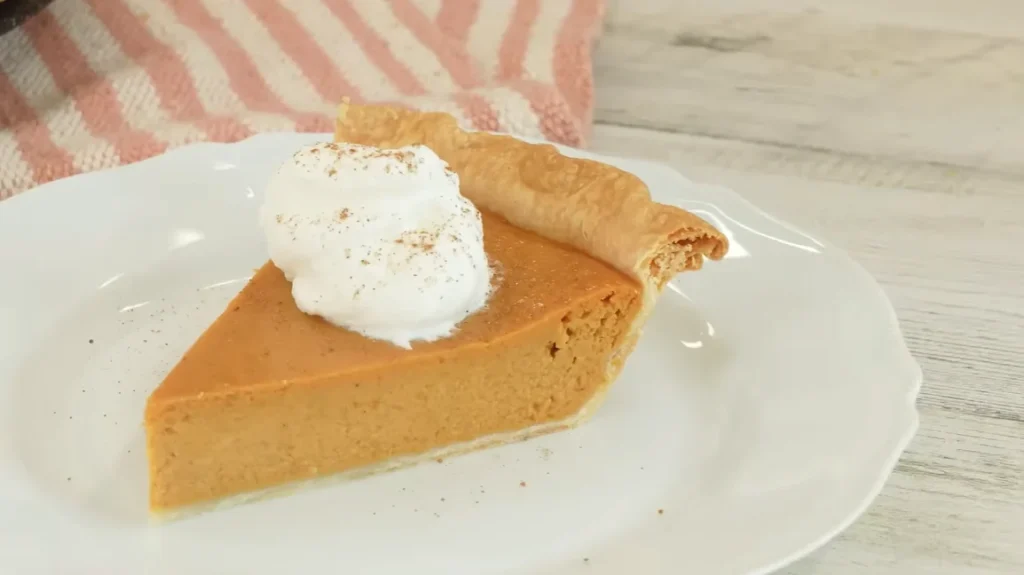 Slice of homemade pumpkin pie topped with whipped cream