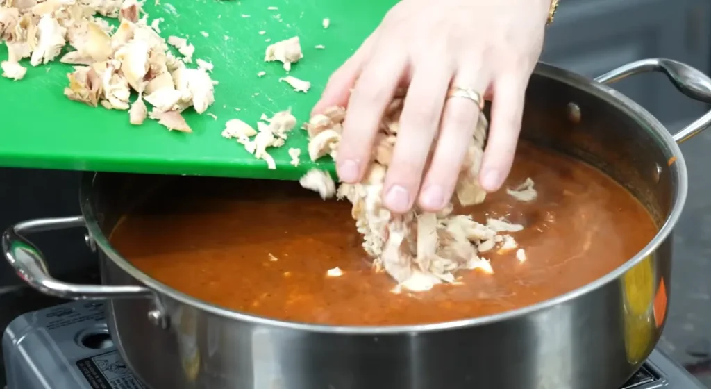 Shredded chicken being added to the creamy tortilla soup
