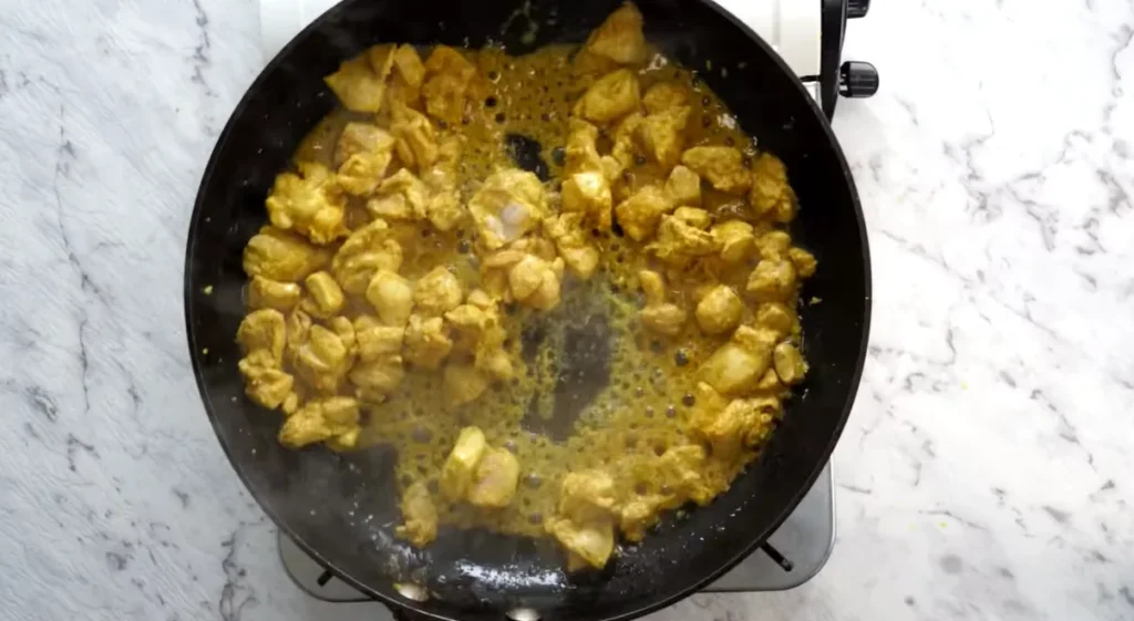 Marinated chicken pieces cooking in a skillet for homemade butter chicken