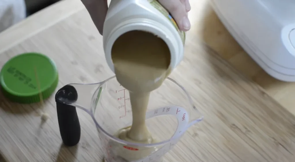 Homemade hummus recipe with smooth tahini being poured into a measuring cup before blending.