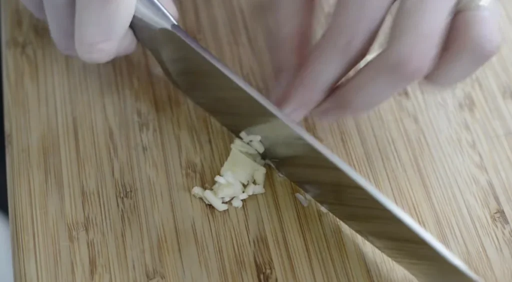 Fresh garlic being finely chopped for a creamy homemade hummus recipe.