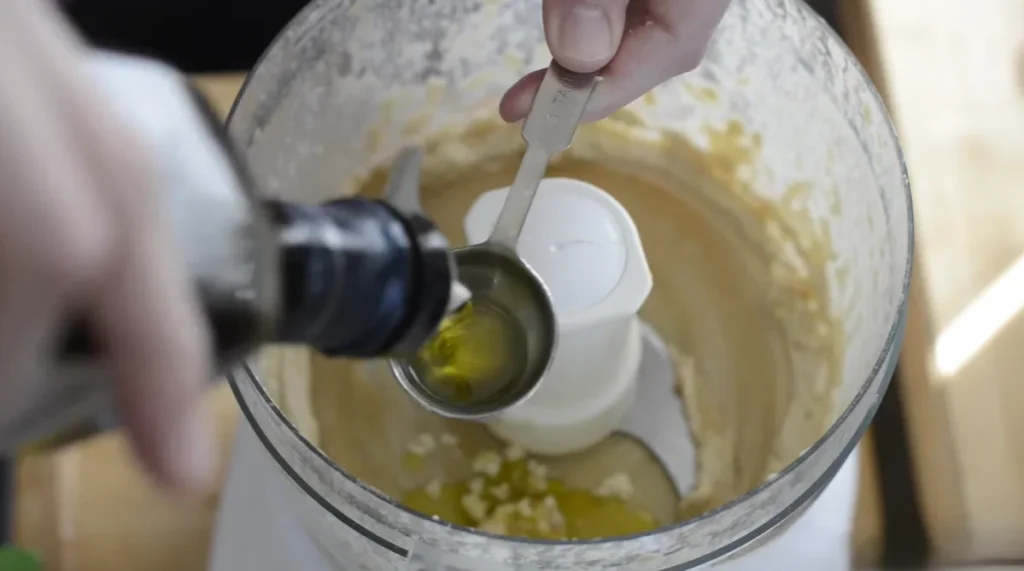 Extra-virgin olive oil being added to homemade hummus ingredients before blending.