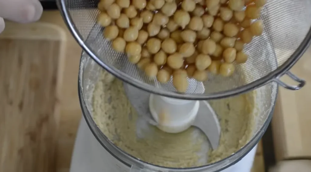 Cooked chickpeas being added to a food processor for homemade hummus.