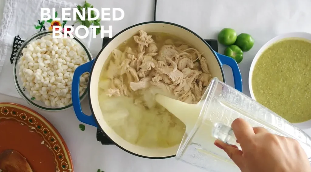 Blended green salsa being added to shredded chicken broth in a Dutch oven
