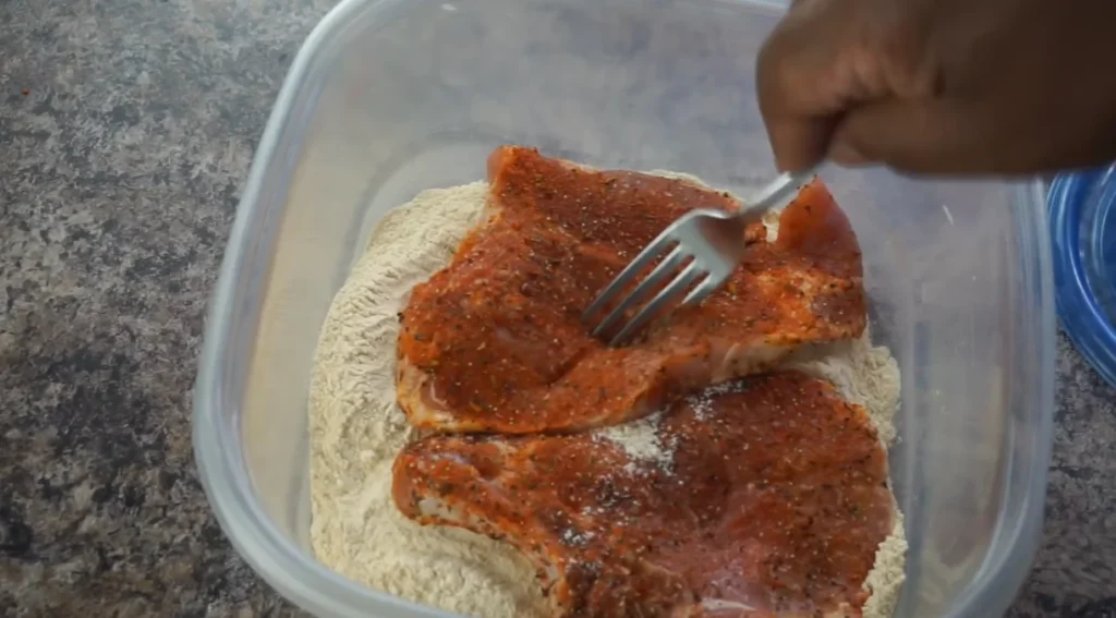 Seasoned bone-in pork chops coated in all-purpose flour before pan-searing for Southern Smothered Pork Chops.