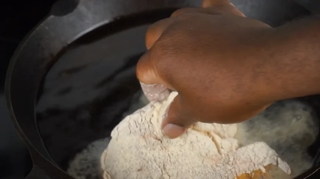 Floured pork chop being placed into a hot skillet with butter and olive oil for a golden-brown crust.