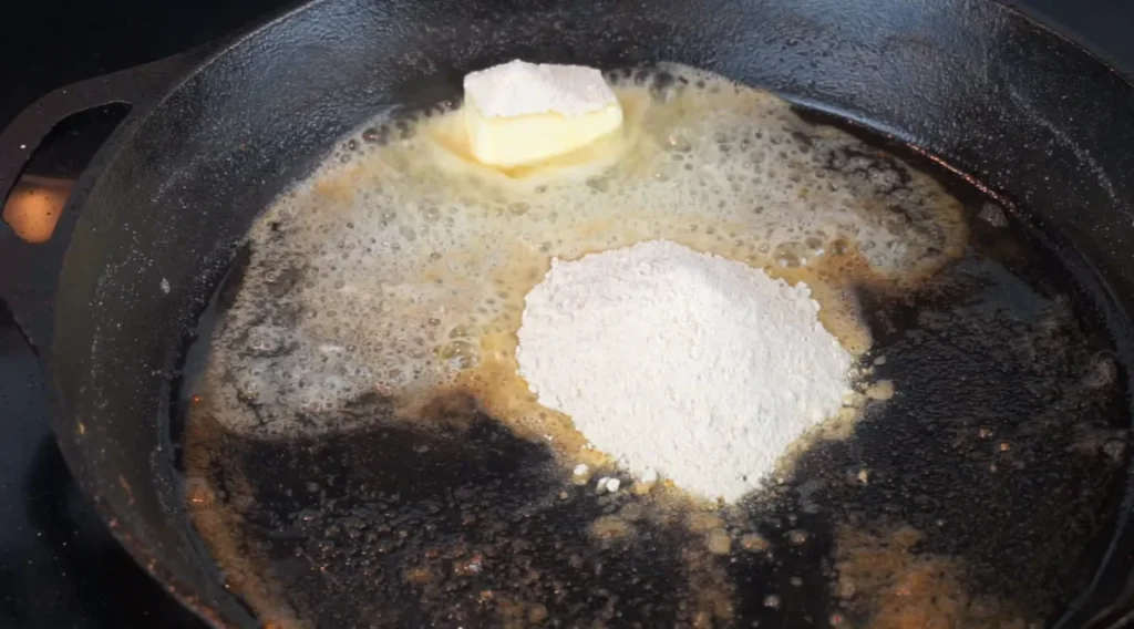 Butter melting with reserved seasoned flour in a cast-iron skillet to create the base for creamy onion gravy.