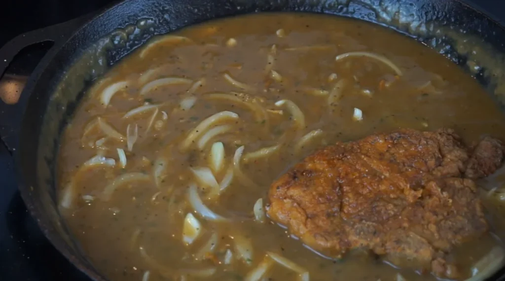 Golden-brown smothered pork chop simmering in creamy onion gravy with tender caramelized onions.