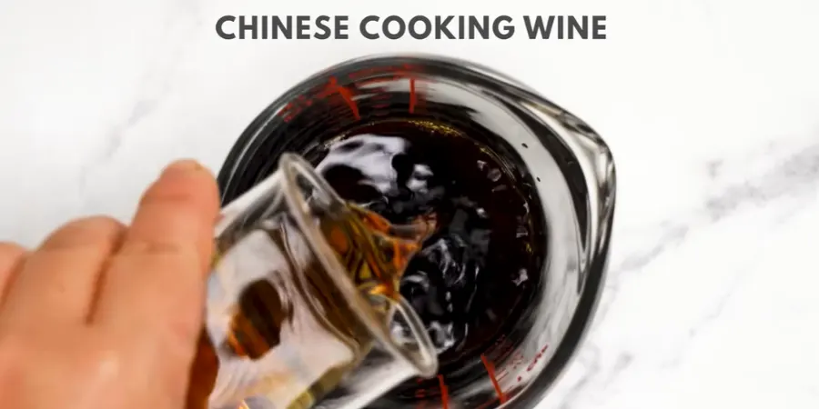 Chinese cooking wine being poured into a glass measuring cup of dark sauce