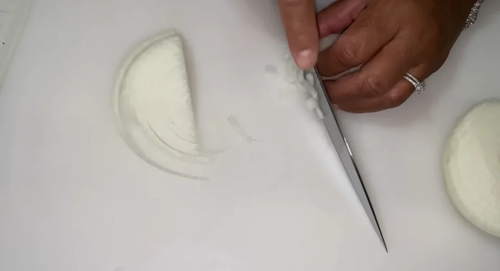 Finely dicing a sweet onion with a chef’s knife on a white cutting board