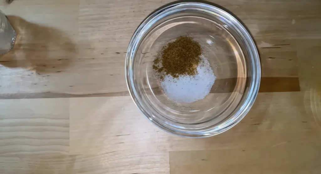 Ground cumin and fine salt in a small glass bowl on a wooden counter