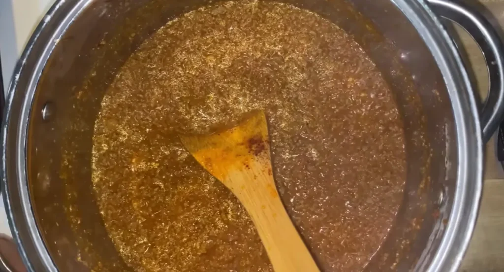 Hot dog chili sauce simmering in a stainless steel pot with a wooden spoon