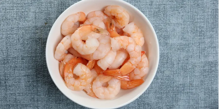 White bowl of peeled shrimp on a blue textured background