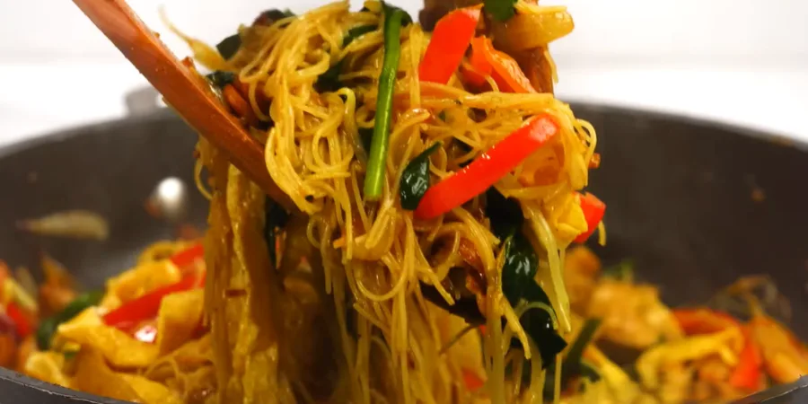 Singapore noodles with thin rice vermicelli, red bell pepper and curry seasoning lifted from a wok with a wooden spoon