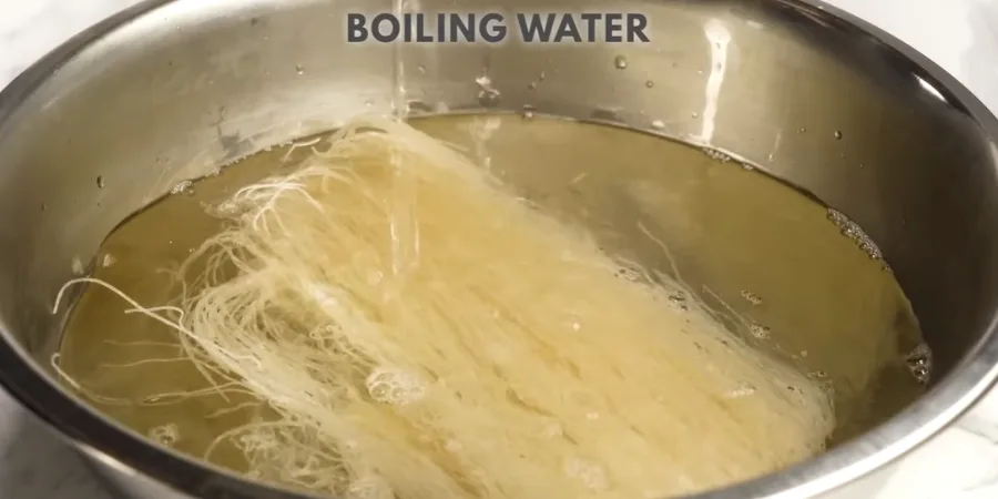 Dried rice vermicelli soaking in hot water in a stainless steel bowl