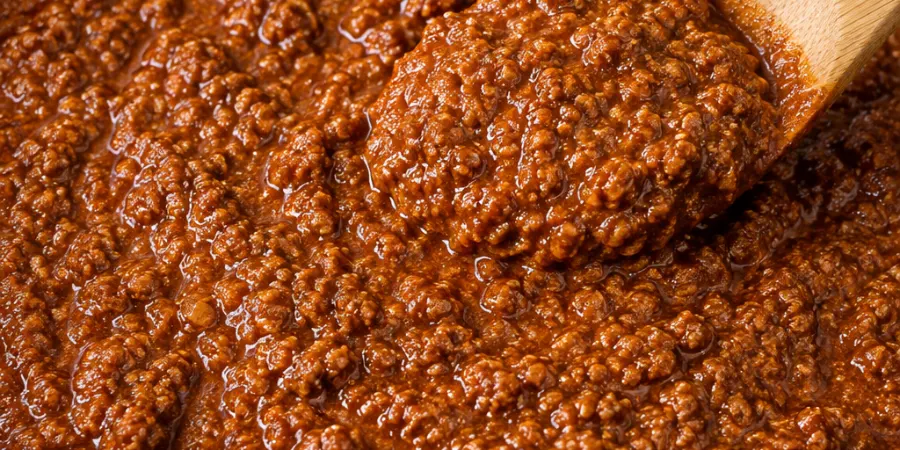 Thick, fine-textured hot dog chili sauce in a black skillet with a wooden spoon