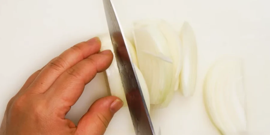 Knife slicing a white onion into thin slices on a white cutting board