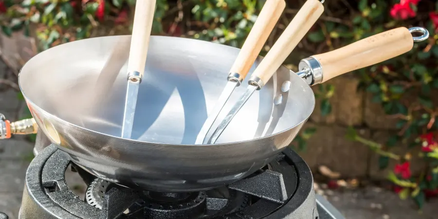 Empty carbon steel wok with wooden handles on a cast iron gas wok burner