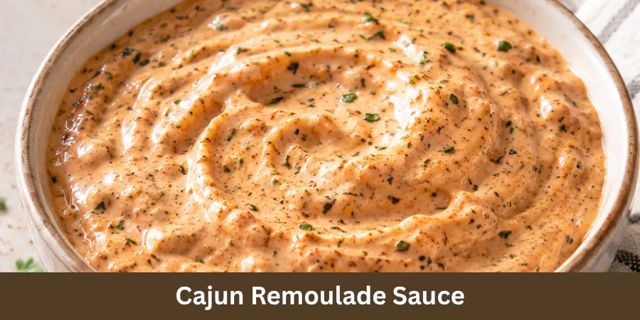 A bowl of creamy Cajun remoulade sauce on a neutral surface with a spoon beside it, shown in a finished food presentation.