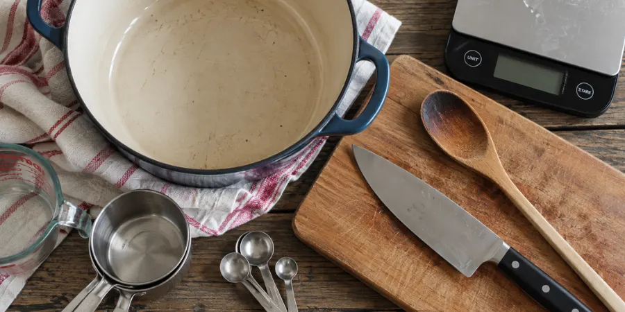 Equipment shot – soup pot, wooden spoon, chef’s knife, cutting board, measuring cups and spoons, and a digital kitchen scale