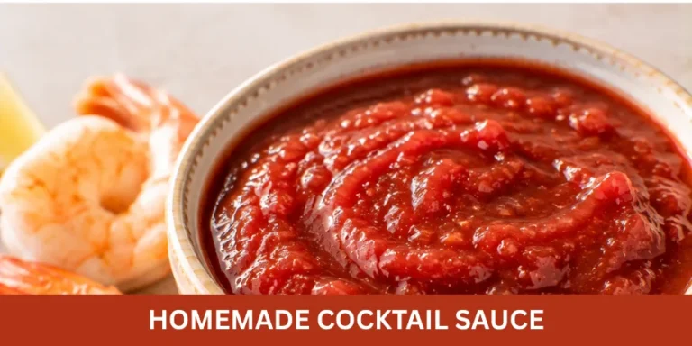 Bowl of homemade cocktail sauce on a neutral serving surface with a small amount of shrimp nearby and a serving utensil.