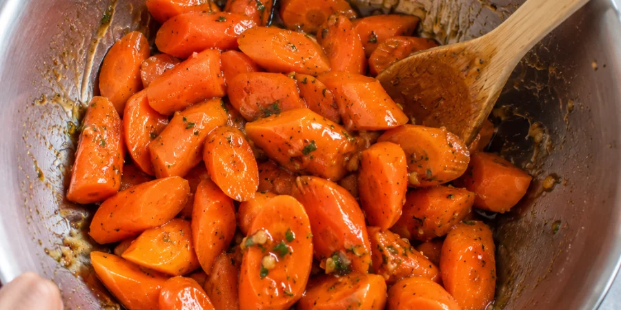 Tossing carrots with honey garlic glaze in a large bowl