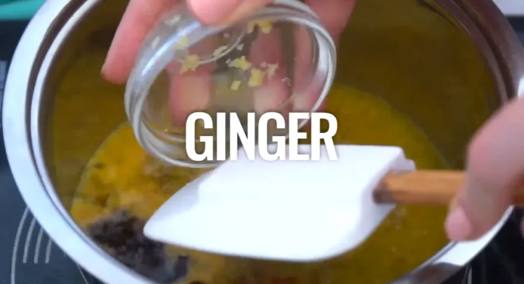 Adding minced fresh ginger to the orange sauce mixture in a saucepan