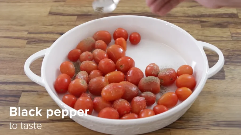 Black pepper being sprinkled over salted cherry tomatoes