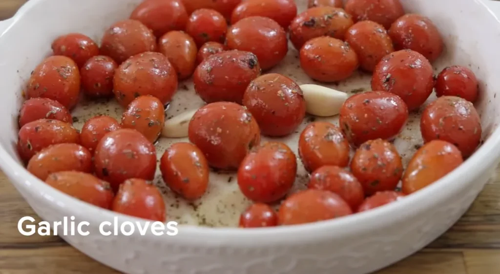 Cherry tomatoes and garlic cloves coated in oil and herbs in a baking dish