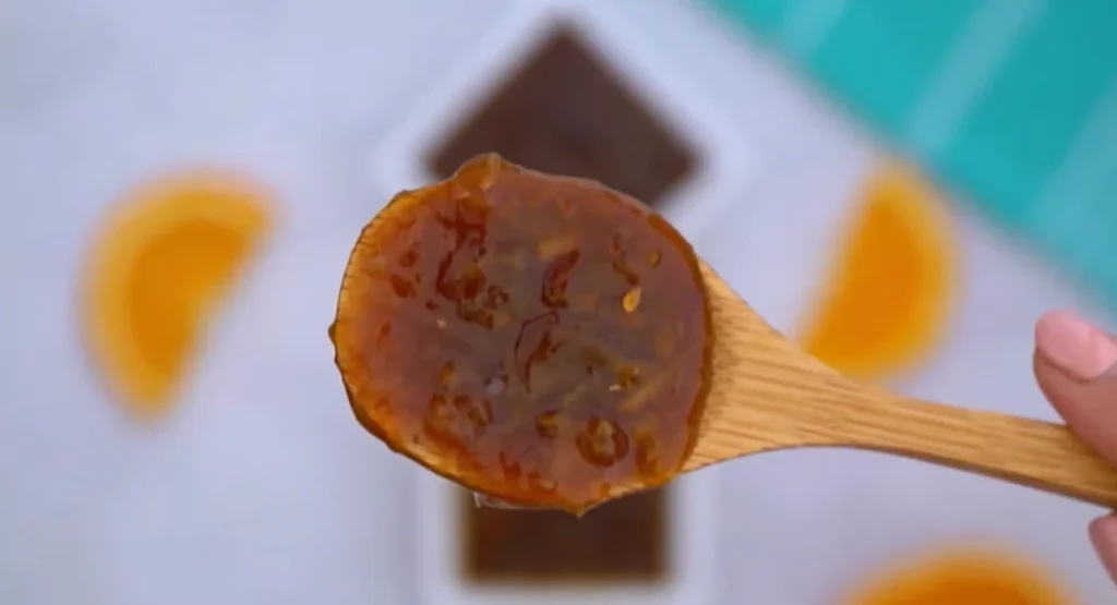 Close-up of a wooden spoon holding glossy orange sauce with bits of zest and ginger