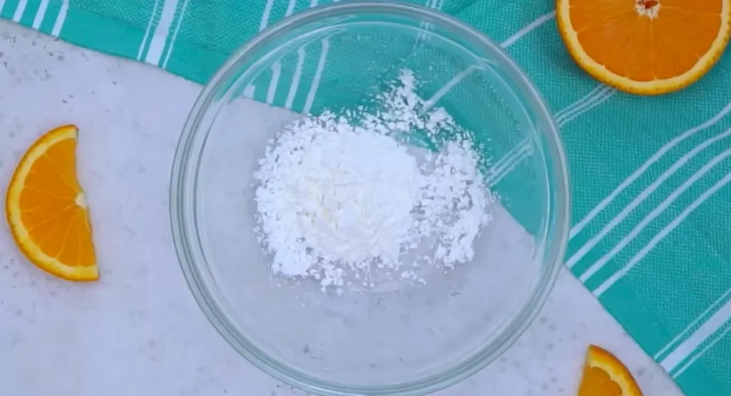 Cornstarch in a clear glass bowl on a marble surface with orange slices around it