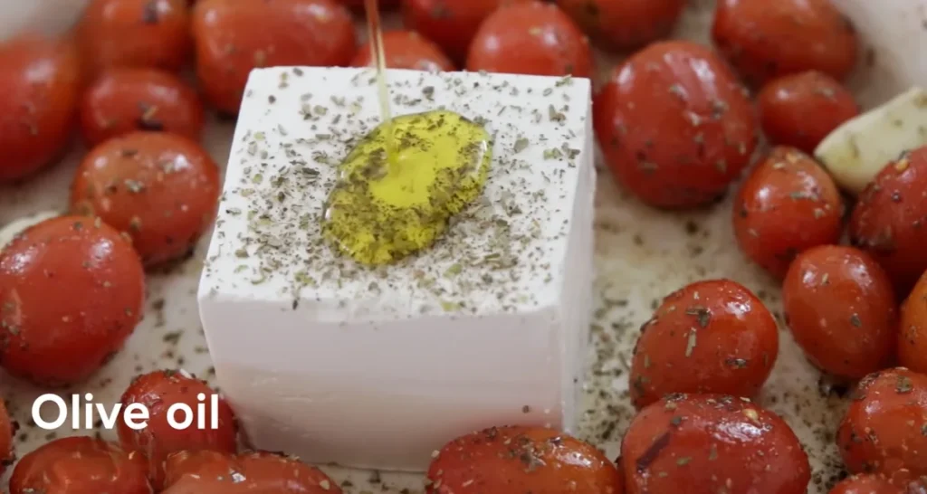 Olive oil being poured over a block of feta topped with dried herbs