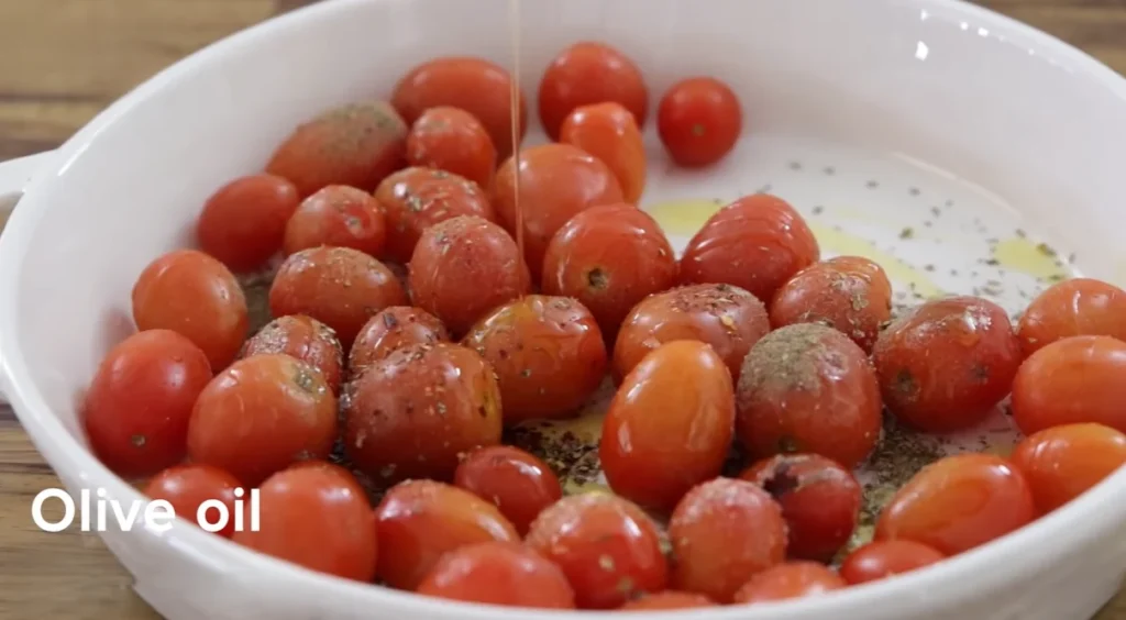 Olive oil drizzling over herb-seasoned cherry tomatoes in a baking dish