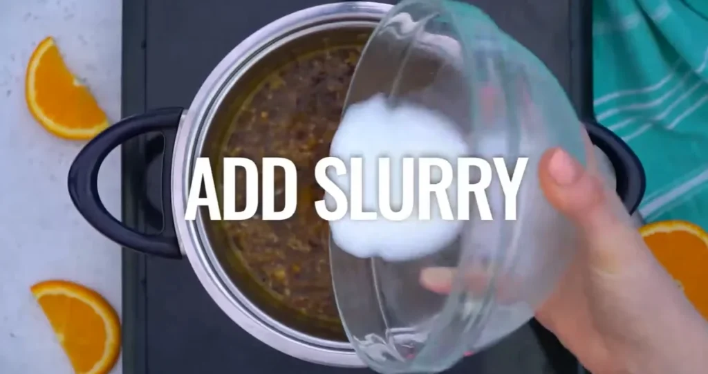 Pouring the cornstarch slurry into the simmering orange sauce in a saucepan