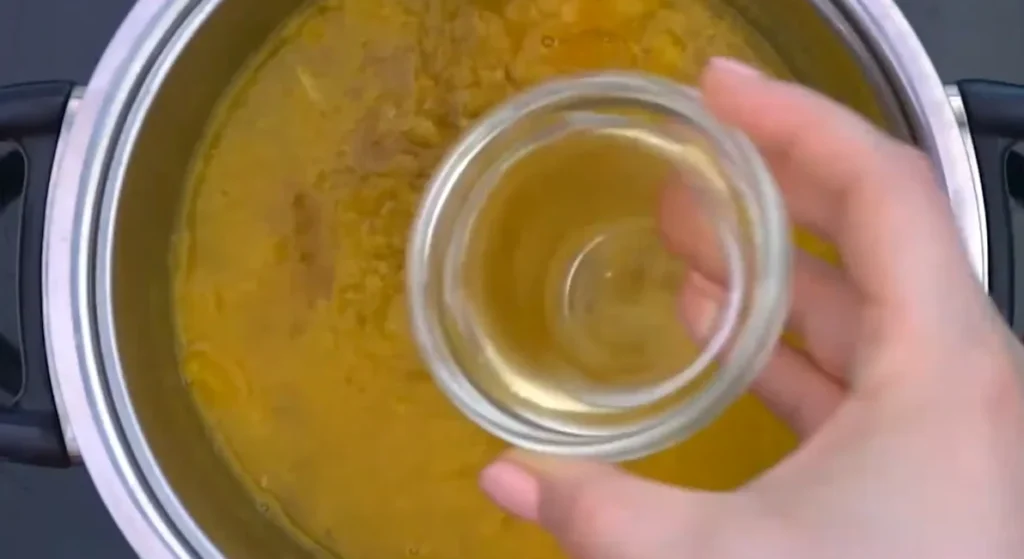 Pouring unseasoned rice vinegar from a small glass bowl into the orange juice in a saucepan
