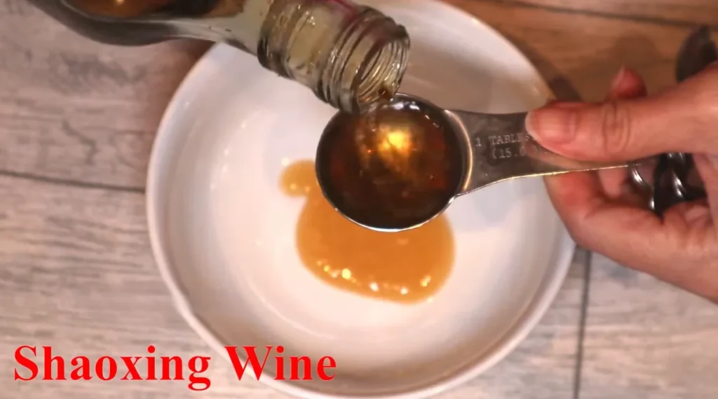 Shaoxing wine being poured into a tablespoon measuring spoon over a white bowl