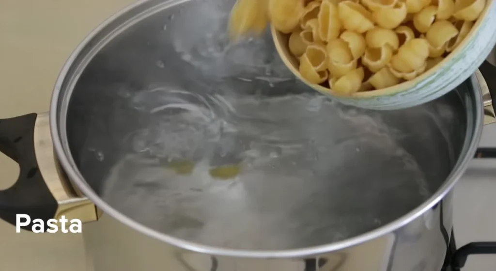 Small shell pasta being poured into a pot of boiling water