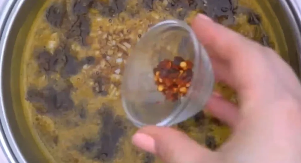 Sprinkling red pepper flakes from a small glass bowl into the orange sauce