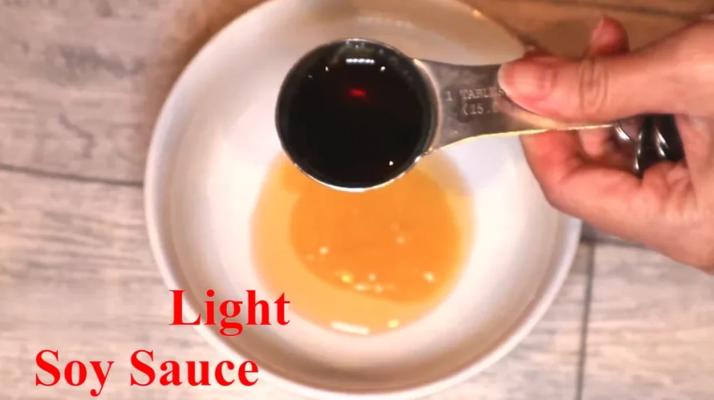 Tablespoon of light soy sauce held over a white bowl with honey in it