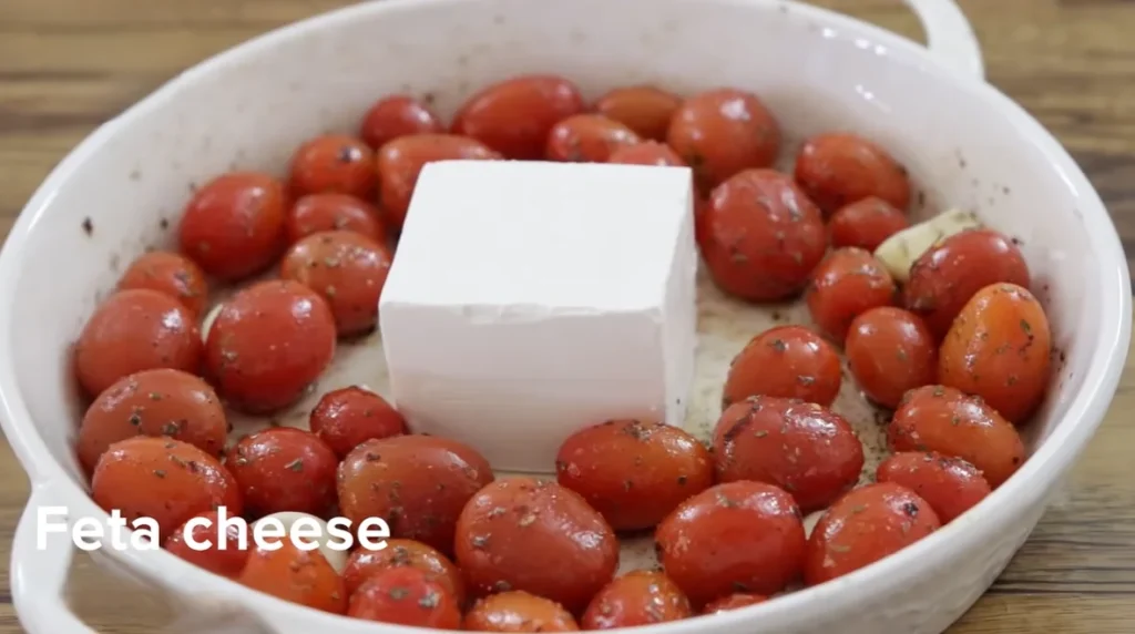 Whole block of feta placed in the center of cherry tomatoes in a white dish